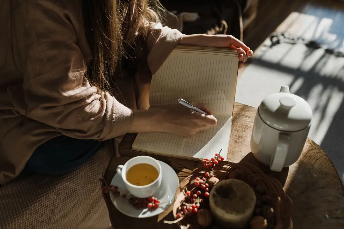 Hands writing privately in a journal beside a cup of tea